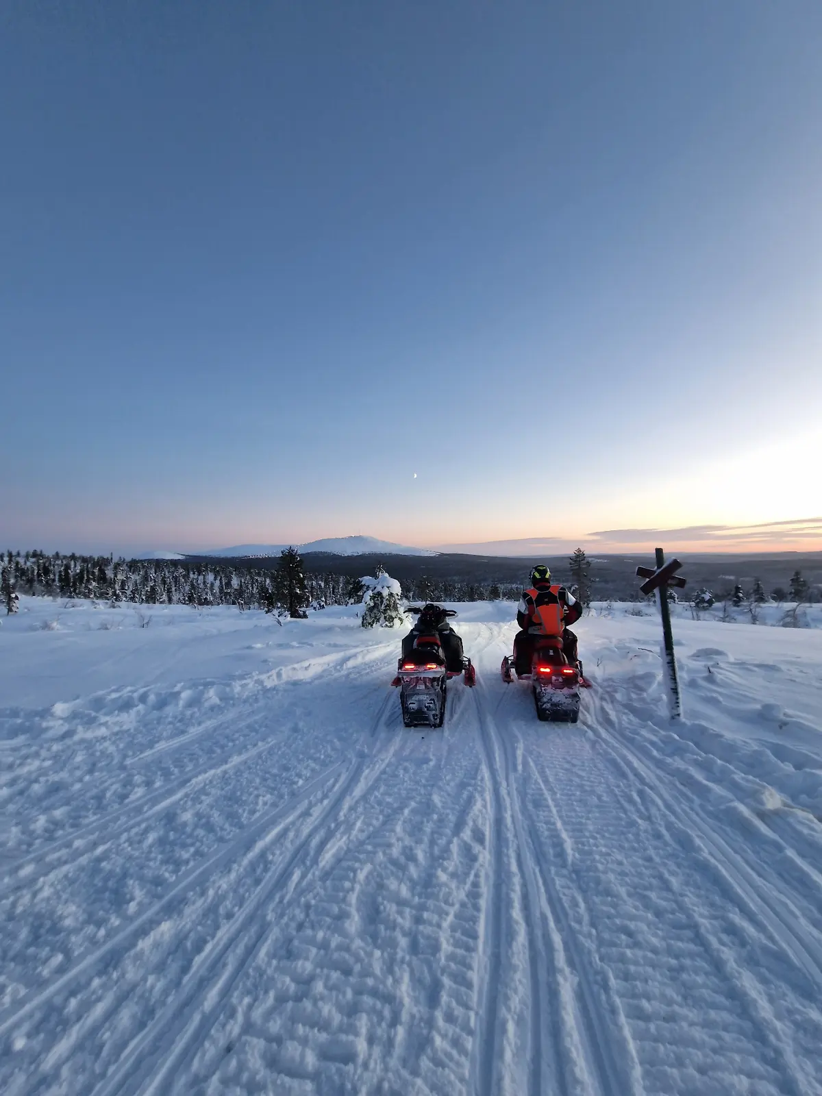 Kaksi moottorikelkkaa tunturireitillä talvisessa iltahämärässä